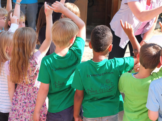 Eine Gruppe von Kindern mit grünen T-Shirts sind von hinten zu sehen und melden sich.