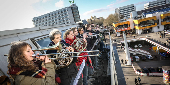 Eine Gruppe Blasmusikerinnen und -musiker steht auf dem Dach der Bibliothek und gibt ein Konzert.