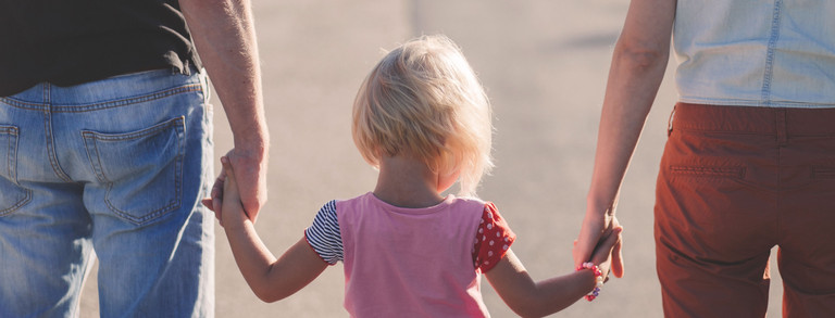 Erwachsene halten ein Kind rechts und links an den Händen.